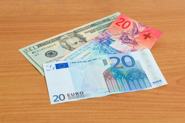 20 USD, 20 CHF and 20 EUR banknotes on wooden table.