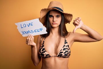 Young beautiful woman on vacation wearing bikini holding paper with love yourself message with...