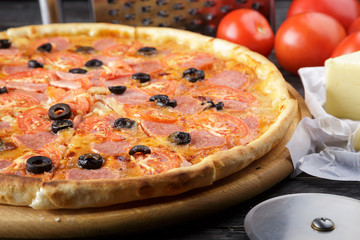 Delicious pizza. Large meat pizza with bacon, sausage, salami, pepperoni and olives. Homemade delicious italian pizza on wooden table for dinner. Italian cuisine.