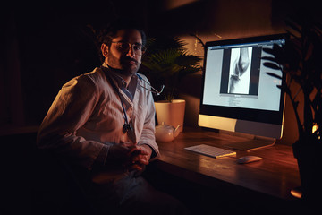 Pensive dilligent intern is working at late night shift at his office using a computer.