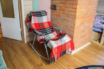 Old wooden rocking chair with a plaid near the stove