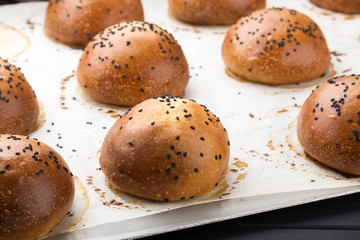 Delicious fresh round buns with sesame seeds on a board. Homemade whole wheat burger buns with sesame seeds on wooden background. 