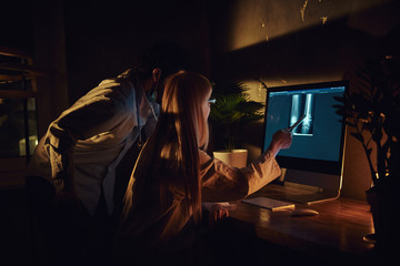 Two busy doctors are looking to the monitor with x-ray screen and have a discussion.
