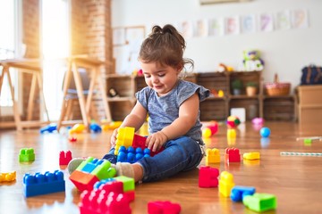 Beautiful toddler sitting on the floor playing with building blocks toys at kindergarten