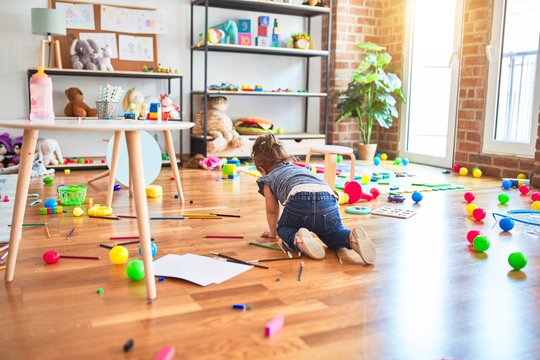 Beautiful toddler crawling on the floor around lots of toys at kindergarten