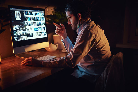 Smart medic in glasses is working with x-ray screens using a computer at dark office.