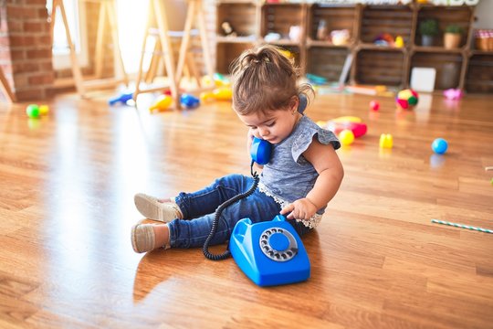 Beautiful toddler sitting on the floor playing with vintage phone at kindergarten