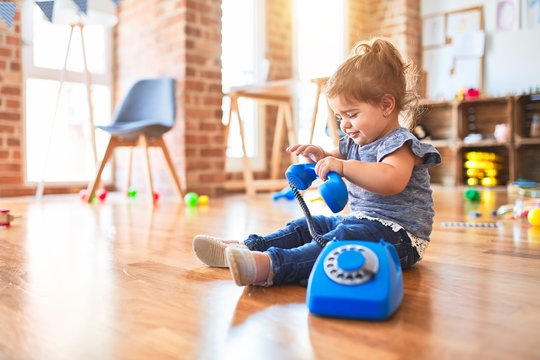 Beautiful toddler sitting on the floor playing with vintage phone at kindergarten