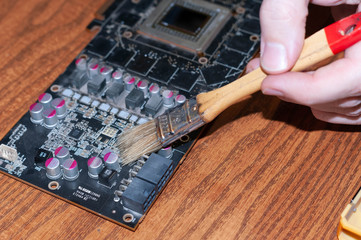 hand of workman cleaning disassembled metal pc card with brush on wooden table in home improvement