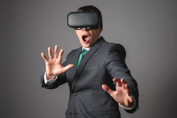 Scared businessman in VR glasses over gray background.