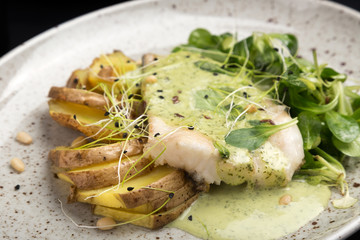 Oven-baked fish. Grilled fish with potatoes, vegetables on a plate on a white table. Delicious roasted fish and potatoes on a white wooden table. Space for text