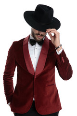 mysterious young man in red velvet tuxedo fixing hat