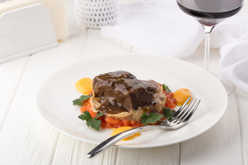 Veal with gravy garnish, vegetables on a white table with wine. Cooked Veal with garnish on white plate. Grill beef tenderloin with barbecue sauce. Space for text, closeup.