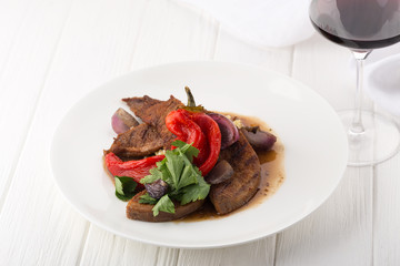 Grilled veal tongue with vegetables on a white table. Cooked tongue. Veal tongue with garnish on white plate. Space for text, closeup.