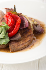 Grilled veal tongue with vegetables on a white table. Cooked tongue. Veal tongue with garnish on white plate. Space for text, closeup.