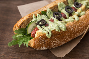 Hot dog with mustard, ketchup and vegetables on wooden table