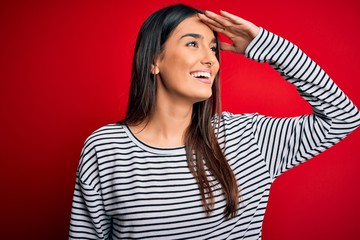 Young beautiful brunette woman wearing casual striped t-shirt over red background very happy and...