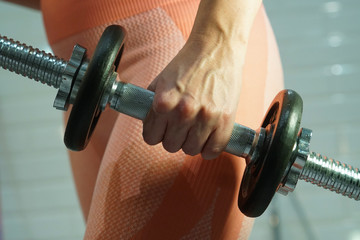 a woman in colorful leggings squeezes a dumbbell in her hand, closeup 