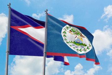 Belize and American Samoa flags waving in the wind against white cloudy blue sky together....