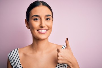 Young beautiful brunette woman wearing casual striped t.shirt over pink background happy with big smile doing ok sign, thumb up with fingers, excellent sign