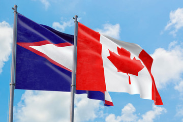 Canada and American Samoa flags waving in the wind against white cloudy blue sky together....