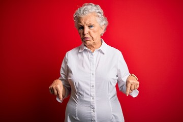 Senior beautiful woman wearing elegant shirt standing over isolated red background Pointing down...