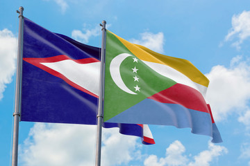 Comoros and American Samoa flags waving in the wind against white cloudy blue sky together....