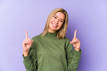 Young blonde caucasian woman isolated indicates with both fore fingers up showing a blank space.