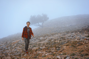 Obraz premium Man in Red Flanel Shirt Hiking in rocky mountains In Thick Fog. Autumn. Tree on Background.