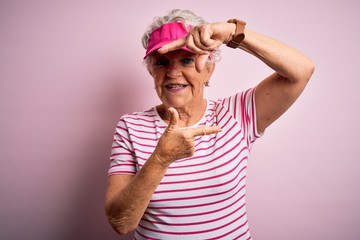 Senior beautiful sporty woman wearing sport cap standing over isolated pink background smiling making frame with hands and fingers with happy face. Creativity and photography concept.