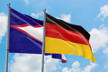 Germany and American Samoa flags waving in the wind against white cloudy blue sky together. Diplomacy concept, international relations.