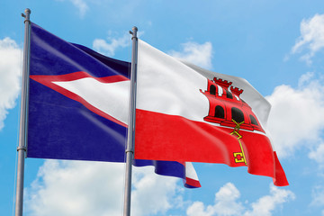 Gibraltar and American Samoa flags waving in the wind against white cloudy blue sky together. Diplomacy concept, international relations.