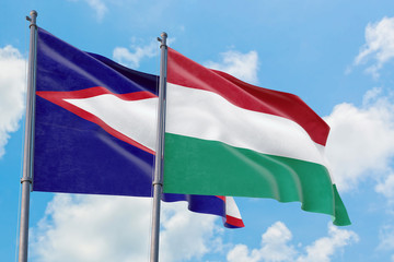 Hungary and American Samoa flags waving in the wind against white cloudy blue sky together. Diplomacy concept, international relations.