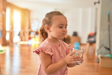 Beautiful blond toddler girl drinking glass of water at kindergarten