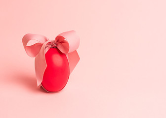 Easter creative concept. One red egg tied with a pink ribbon on a pink background. Minimalism, copy space, close up