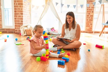 Beautiful psycologist and blond toddler girl doing therapy building tower using plastic blocks at...