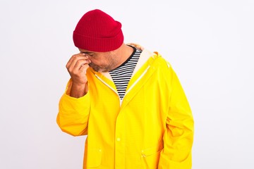 Middle age man wearing rain coat and woolen hat standing over isolated white background tired rubbing nose and eyes feeling fatigue and headache. Stress and frustration concept.