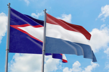 Netherlands and American Samoa flags waving in the wind against white cloudy blue sky together. Diplomacy concept, international relations.