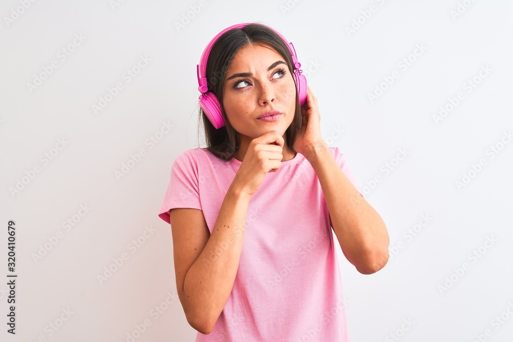 Poster Young beautiful woman listening to music using headphones over isolated white background serious face thinking about question, very confused idea