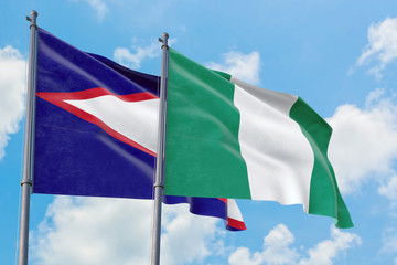Nigeria and American Samoa flags waving in the wind against white cloudy blue sky together. Diplomacy concept, international relations.
