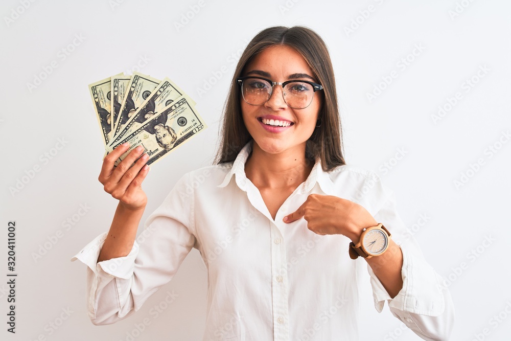 Wall mural Beautiful businesswoman wearing glasses holding dollars over isolated white background with surprise face pointing finger to himself - Wall murals