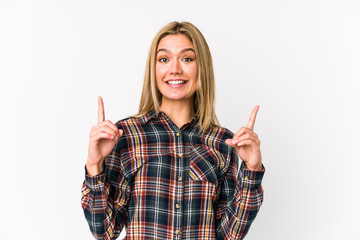 Young blonde caucasian woman isolated indicates with both fore fingers up showing a blank space.
