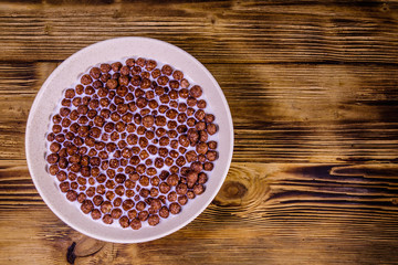 Ceramic plate with chocolate cereal balls in milk on wooden table. Top view