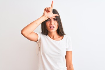 Young beautiful woman wearing casual t-shirt standing over isolated white background making fun of people with fingers on forehead doing loser gesture mocking and insulting.