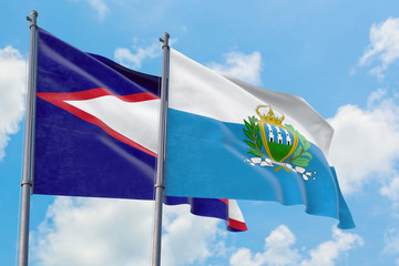 San Marino and American Samoa flags waving in the wind against white cloudy blue sky together. Diplomacy concept, international relations.