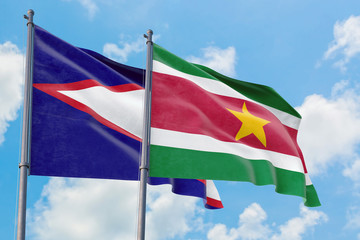 Suriname and American Samoa flags waving in the wind against white cloudy blue sky together. Diplomacy concept, international relations.