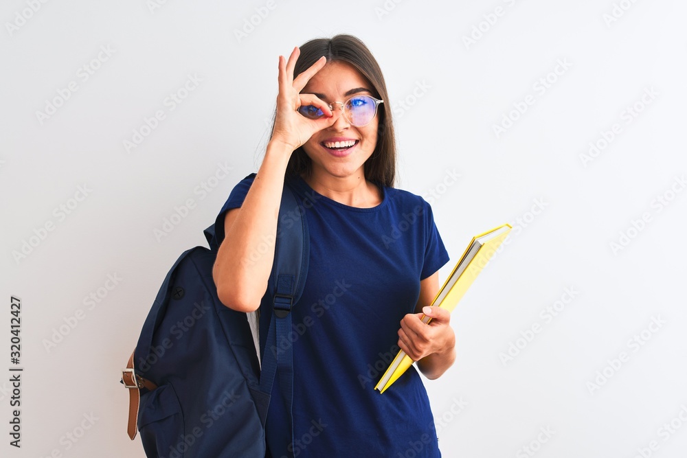 Wall mural Young student woman wearing backpack glasses holding book over isolated white background with happy face smiling doing ok sign with hand on eye looking through fingers - Wall murals