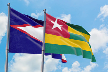 Togo and American Samoa flags waving in the wind against white cloudy blue sky together. Diplomacy concept, international relations.