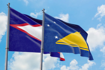 Tokelau and American Samoa flags waving in the wind against white cloudy blue sky together. Diplomacy concept, international relations.