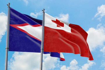 Tonga and American Samoa flags waving in the wind against white cloudy blue sky together. Diplomacy concept, international relations.